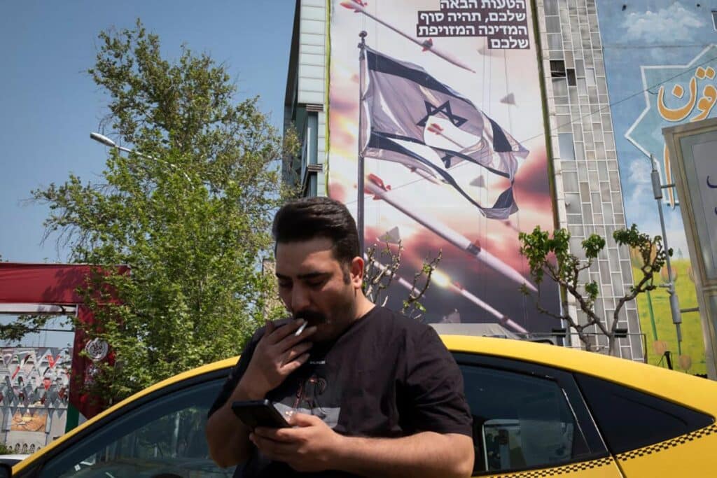 An Iranian yellow cab driver using his cellphone while standing under an anti-Israeli mural, which displays the IRGC missile and UAV attack on Israel, in downtown Tehran, Iran, on April 14, 2024. Iran launched dozens of Unmanned Aerial Vehicles (UAVs) and missiles against Israel in response to the attack on its Consulate in Damascus.