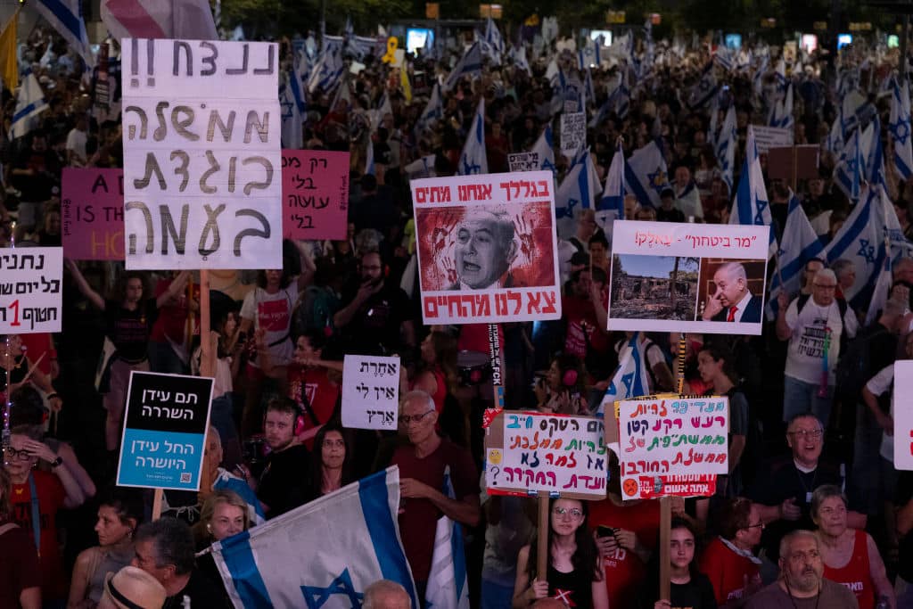 TEL AVIV, ISRAEL - AUGUST 24: Protesters hold signs and flags during a demonstration calling for a hostage deal and against Israeli Prime Minister Benjamin Netanyahu and his government on August 24, 2024 in Tel Aviv, Israel. Earlier today, Hamas said it was sending a delegation to Cairo where mediators from the United States, Qatar and Egypy intend to continue ceasefire talks. One main sticking point is Israel's insistence on leaving troops along the Gaza-Egypt border, which both Egypt and Hamas object to. (Photo by Amir Levy/Getty Images)