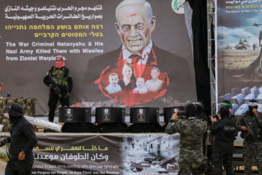 Masked Palestinian militants stand next to one of the coffins on stage, with an altered portrait of Israeli Premier Benjamin Netanyahu in the background, before handing over the bodies of four Israeli hostages to the Red Cross in Khan Yunis in the southern Gaza on February 20, 2025. Hamas handed over on February 20 coffins believed to contain the bodies of four Israeli hostages, including those of the Bibas family who became symbols of the ordeal that has gripped Israel since the Gaza war began. The transfer of the bodies is the first by Hamas since its October 7, 2023 attack on Israel triggered the war, and is taking place under a fragile ceasefire that has seen living hostages exchanged for Palestinians held in Israeli prisons. (Photo by Saeed Jaras / Middle East Images / Middle East Images via AFP) (Photo by SAEED JARAS/Middle East Images/AFP via Getty Images)