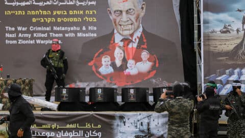 Masked Palestinian militants stand next to one of the coffins on stage, with an altered portrait of Israeli Premier Benjamin Netanyahu in the background, before handing over the bodies of four Israeli hostages to the Red Cross in Khan Yunis in the southern Gaza on February 20, 2025. Hamas handed over on February 20 coffins believed to contain the bodies of four Israeli hostages, including those of the Bibas family who became symbols of the ordeal that has gripped Israel since the Gaza war began. The transfer of the bodies is the first by Hamas since its October 7, 2023 attack on Israel triggered the war, and is taking place under a fragile ceasefire that has seen living hostages exchanged for Palestinians held in Israeli prisons. (Photo by Saeed Jaras / Middle East Images / Middle East Images via AFP) (Photo by SAEED JARAS/Middle East Images/AFP via Getty Images)