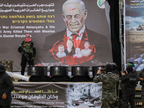 Masked Palestinian militants stand next to one of the coffins on stage, with an altered portrait of Israeli Premier Benjamin Netanyahu in the background, before handing over the bodies of four Israeli hostages to the Red Cross in Khan Yunis in the southern Gaza on February 20, 2025. Hamas handed over on February 20 coffins believed to contain the bodies of four Israeli hostages, including those of the Bibas family who became symbols of the ordeal that has gripped Israel since the Gaza war began. The transfer of the bodies is the first by Hamas since its October 7, 2023 attack on Israel triggered the war, and is taking place under a fragile ceasefire that has seen living hostages exchanged for Palestinians held in Israeli prisons. (Photo by Saeed Jaras / Middle East Images / Middle East Images via AFP) (Photo by SAEED JARAS/Middle East Images/AFP via Getty Images)