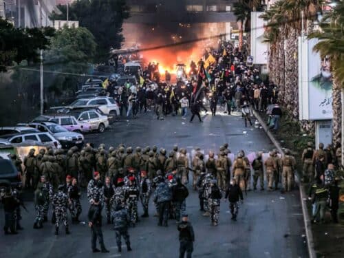 Fire from burning tires burns as supporters of Lebanese Shiite Islamist movement Hezbollah stand before Lebanese Army soldiers during a Hezbollah-organised rally to block the road to Beirut International Airport over a decision to bar two Iranian flights from landing there, in Beirut on February 15, 2025.